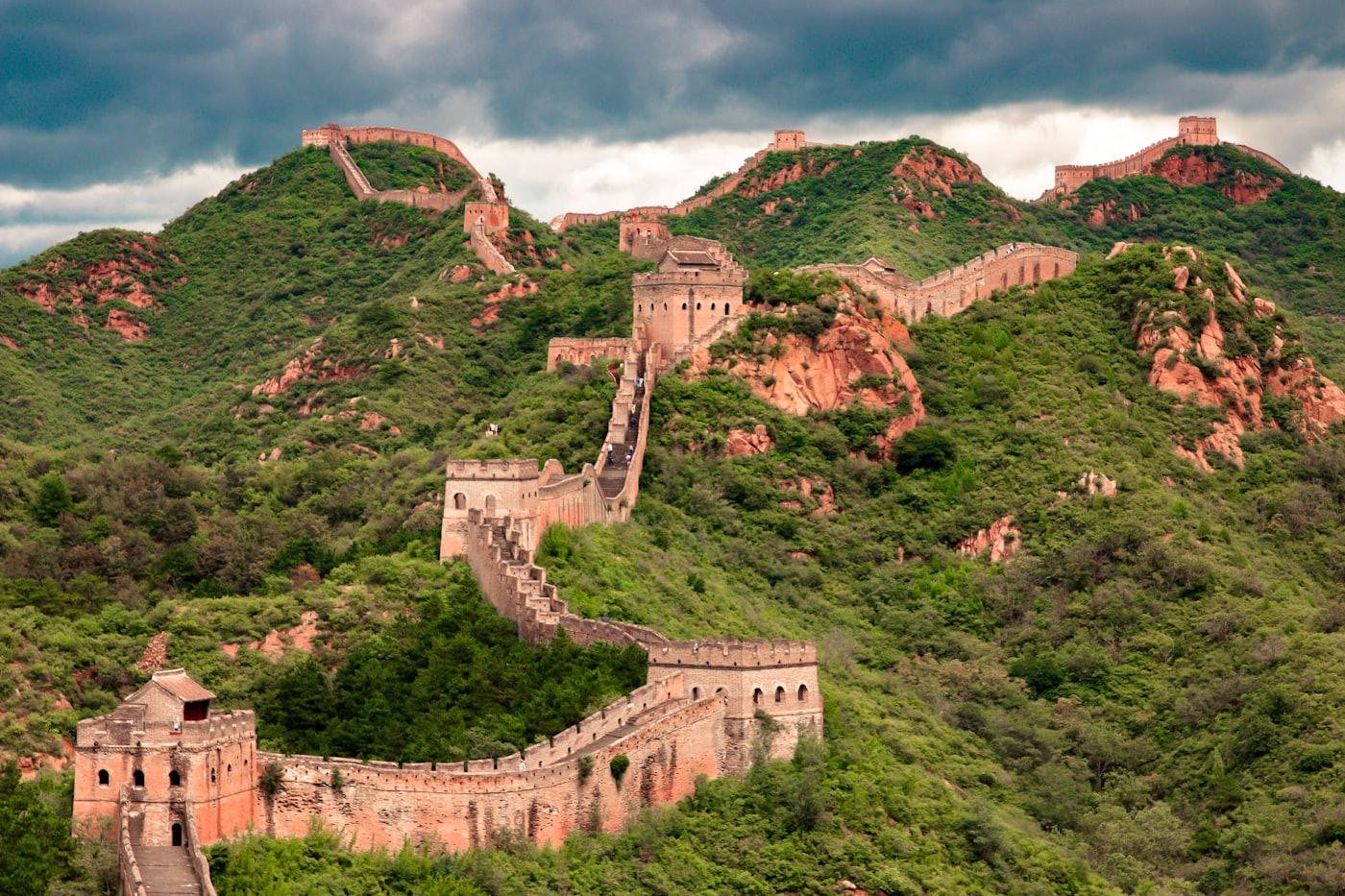 The Great Wall of China snaking over green ridges under storm clouds