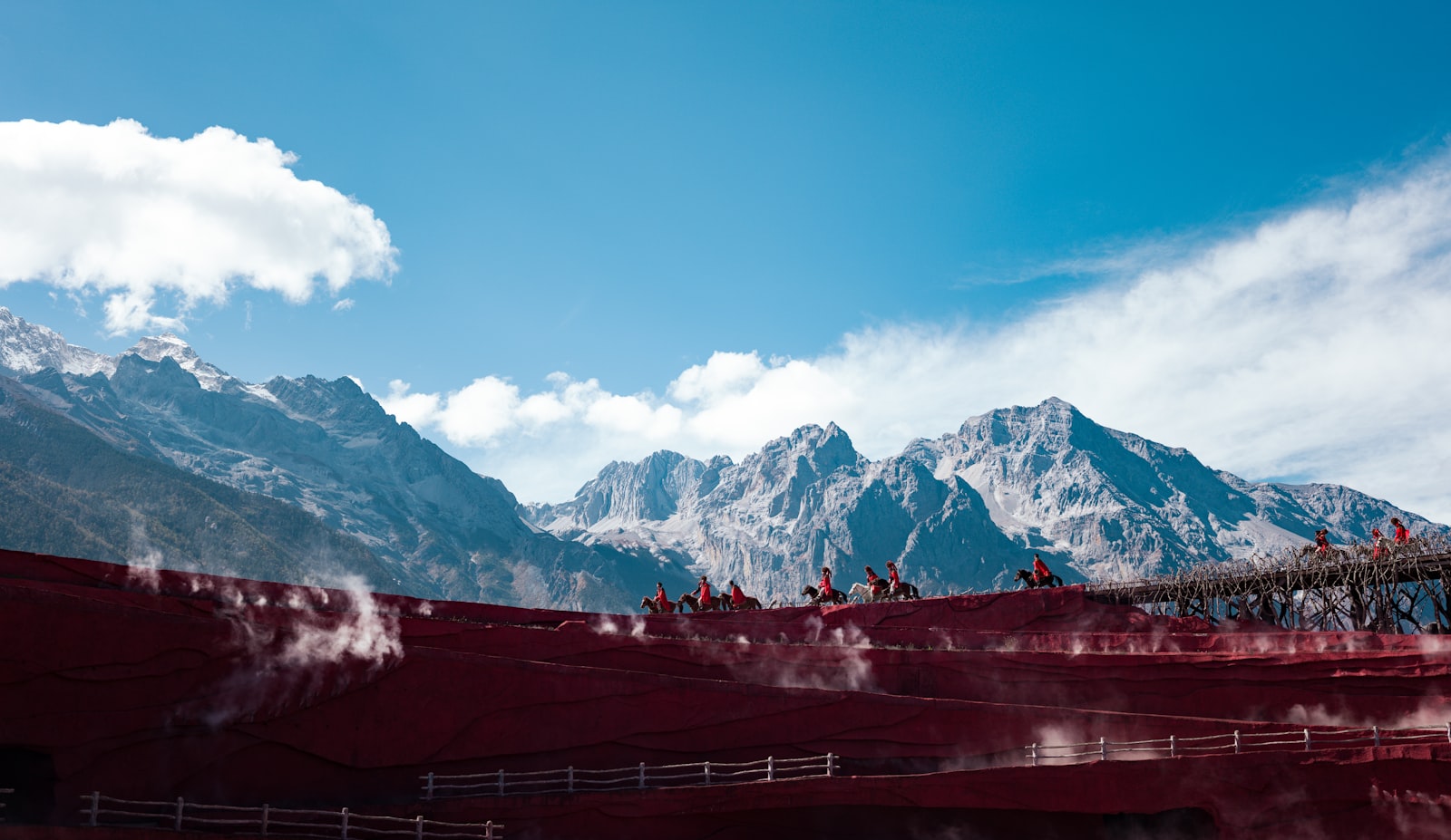 Horsemen riding across red terraces with the Jade Dragon Snow Mountain behind, Lijiang